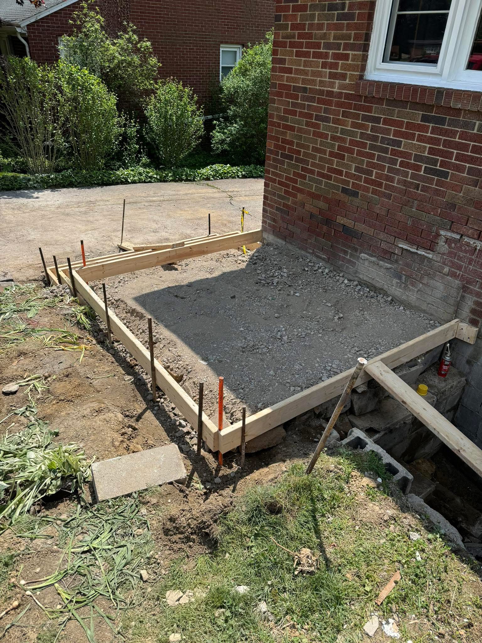Formed footer and slab against a brick house with compacted gravel base and rebar